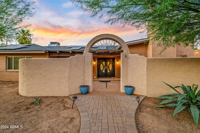 exterior entry at dusk featuring solar panels and stucco siding