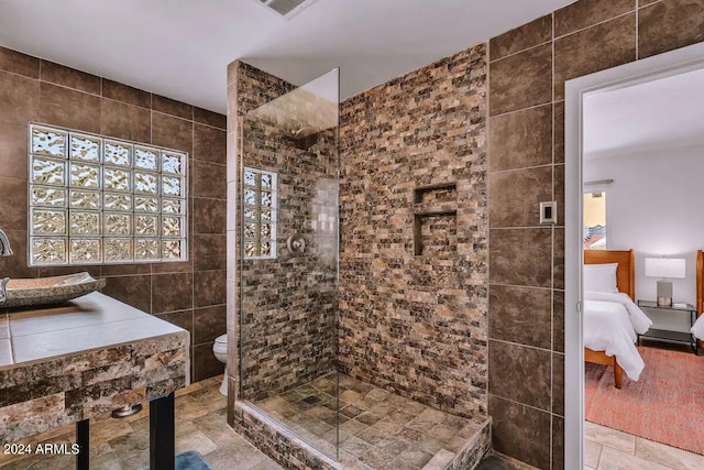 full bath featuring toilet, stone tile flooring, tile walls, walk in shower, and ensuite bathroom