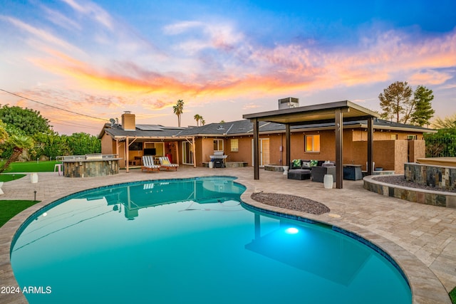 pool at dusk with a patio, a hot tub, a grill, and an outdoor living space