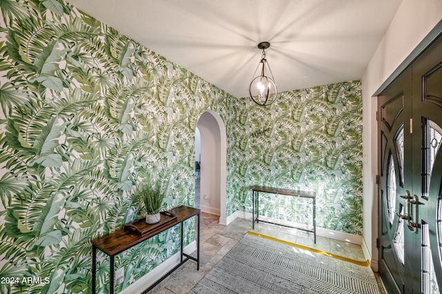 foyer with arched walkways, a chandelier, wallpapered walls, and baseboards