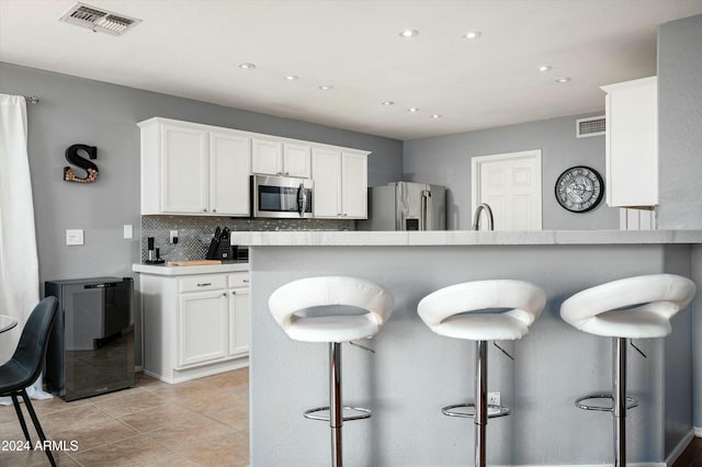 kitchen featuring kitchen peninsula, backsplash, a breakfast bar, stainless steel appliances, and white cabinetry