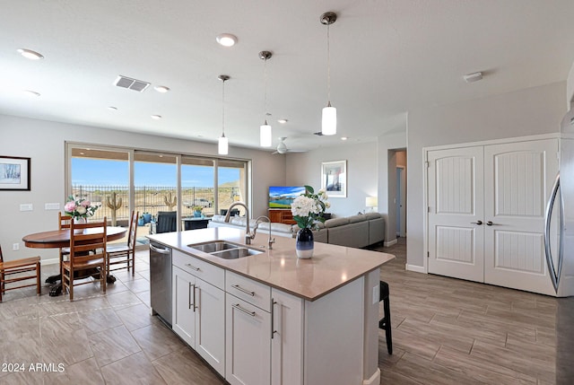 kitchen featuring sink, white cabinetry, decorative light fixtures, stainless steel dishwasher, and an island with sink