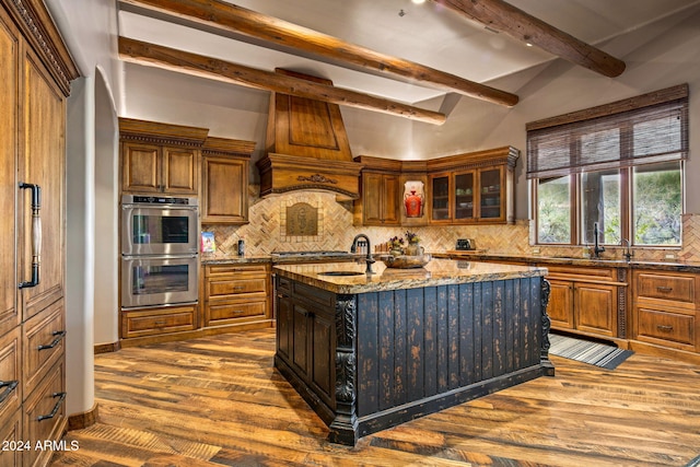 kitchen with backsplash, a kitchen island with sink, and double oven