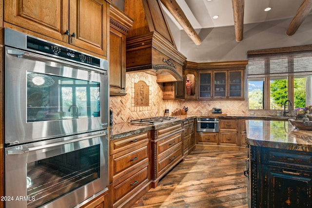 kitchen featuring lofted ceiling with beams, dark stone counters, decorative backsplash, appliances with stainless steel finishes, and hardwood / wood-style flooring