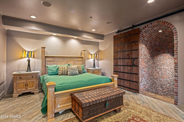 bedroom featuring a barn door, light hardwood / wood-style flooring, and brick wall