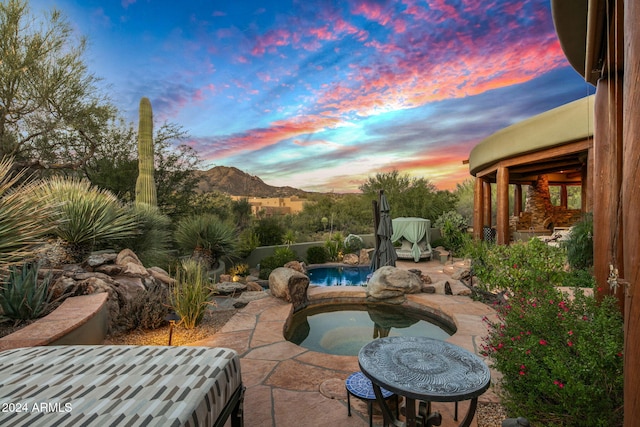 patio terrace at dusk with a mountain view and a pool with hot tub