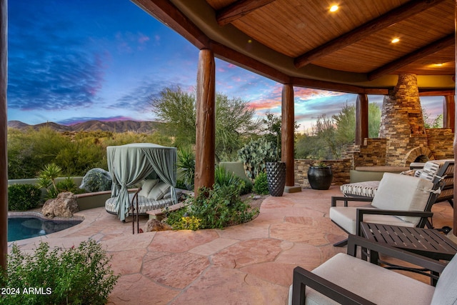 patio terrace at dusk with an outdoor stone fireplace and a mountain view