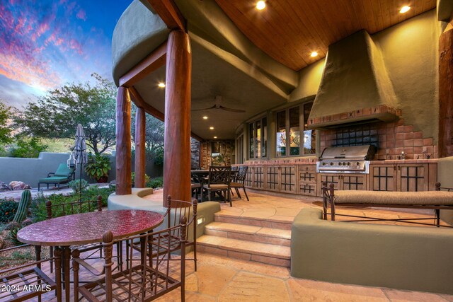 patio terrace at dusk with area for grilling, ceiling fan, and exterior kitchen