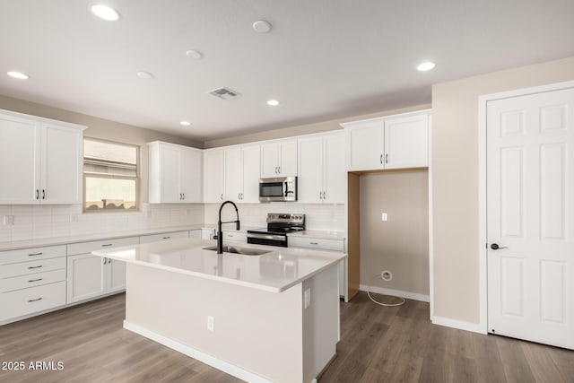 kitchen with appliances with stainless steel finishes, white cabinetry, sink, hardwood / wood-style flooring, and a center island with sink