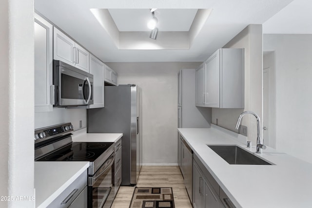 kitchen featuring gray cabinetry, a raised ceiling, sink, light wood-type flooring, and appliances with stainless steel finishes