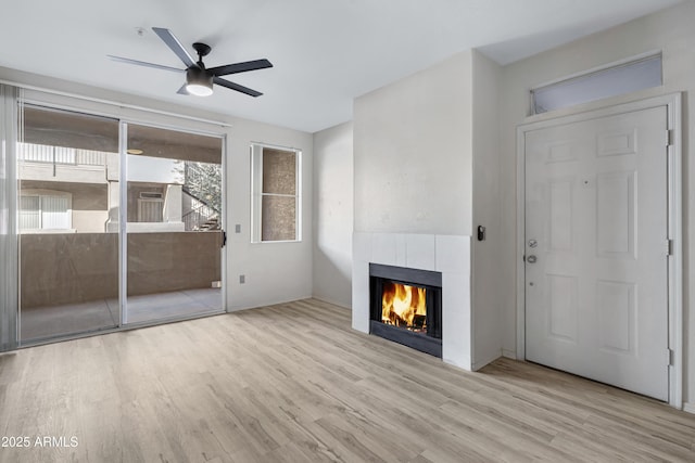 unfurnished living room with light hardwood / wood-style flooring, ceiling fan, and a tiled fireplace