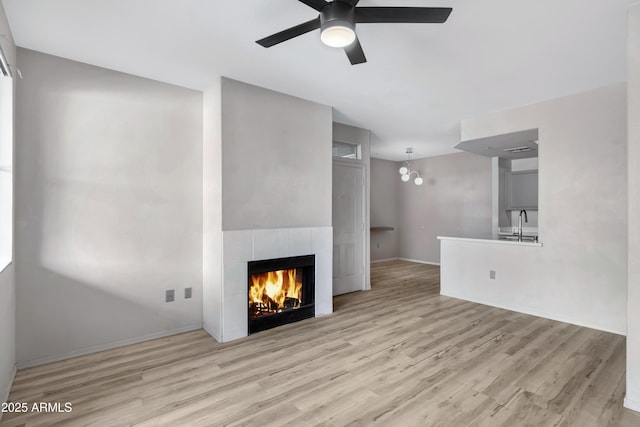 unfurnished living room with ceiling fan with notable chandelier, light hardwood / wood-style floors, sink, and a fireplace