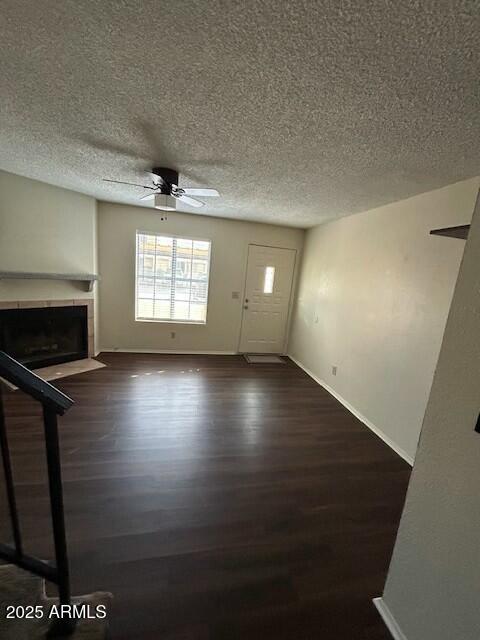 unfurnished living room featuring a tile fireplace, a ceiling fan, wood finished floors, a textured ceiling, and baseboards