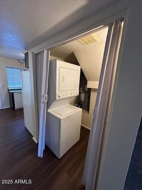 laundry room with dark wood finished floors, a textured ceiling, visible vents, stacked washer / dryer, and laundry area