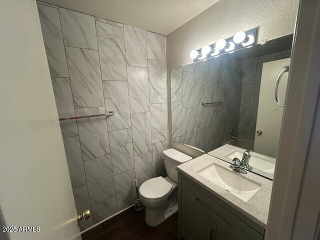 bathroom with tile walls, a textured ceiling, toilet, tiled shower, and vanity