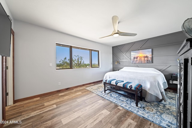 bedroom with baseboards, an accent wall, wood finished floors, and a ceiling fan