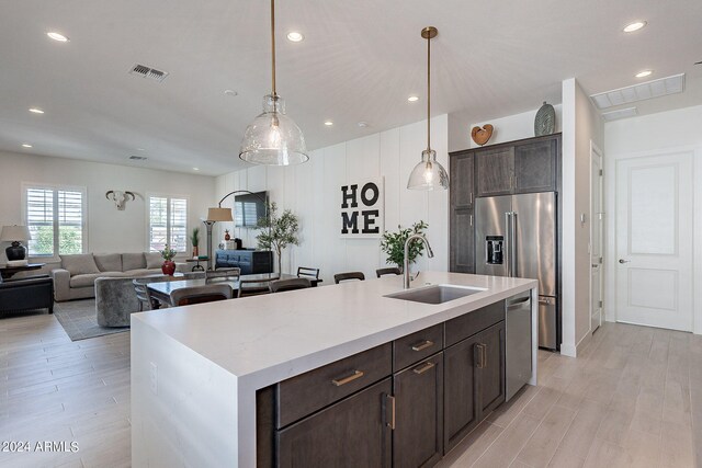 kitchen featuring appliances with stainless steel finishes, a center island with sink, light hardwood / wood-style floors, and sink