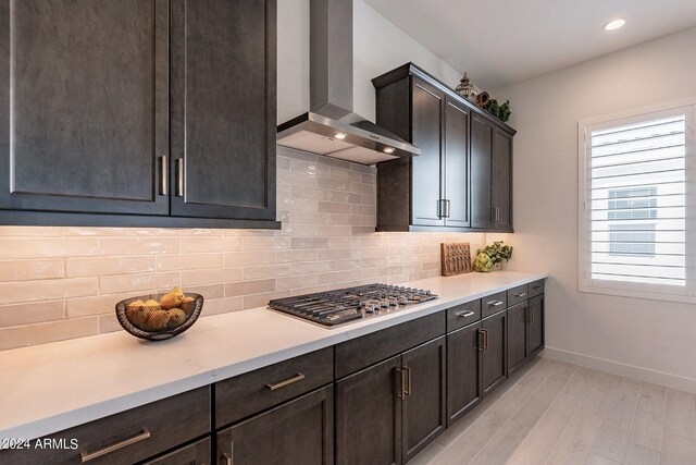 kitchen featuring light hardwood / wood-style floors, tasteful backsplash, stainless steel gas stovetop, wall chimney exhaust hood, and dark brown cabinetry