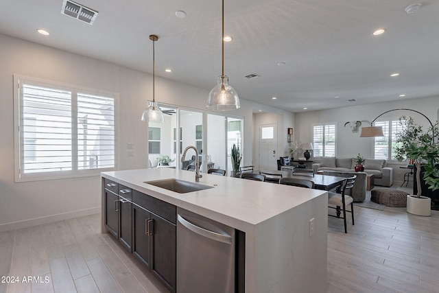 kitchen featuring light hardwood / wood-style floors, dishwasher, decorative light fixtures, a kitchen island with sink, and sink