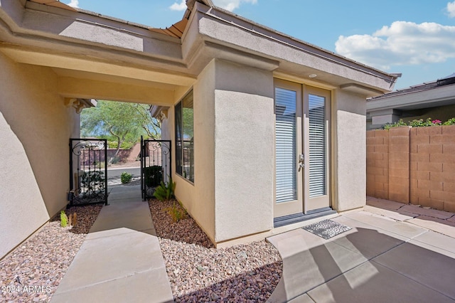 property entrance with a gate, french doors, fence, and stucco siding