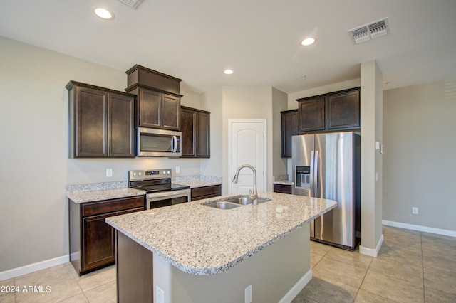 kitchen with light stone counters, a center island with sink, stainless steel appliances, and sink