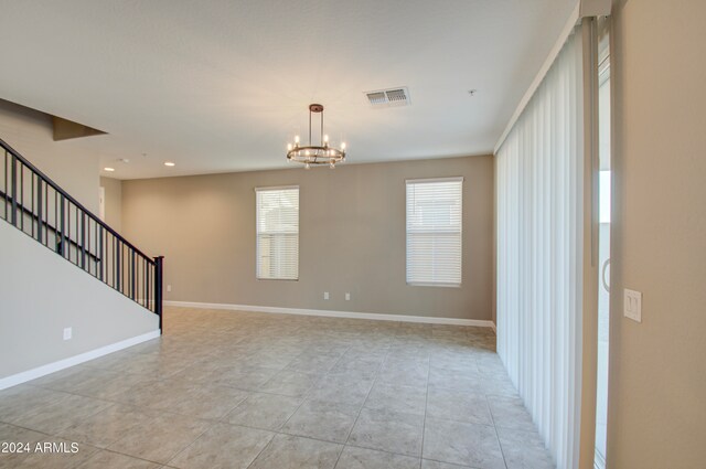 empty room featuring a notable chandelier and light tile patterned flooring