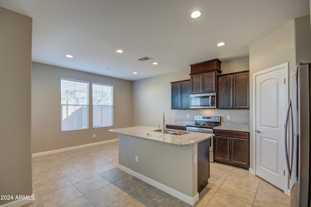 kitchen with dark brown cabinetry, an island with sink, sink, appliances with stainless steel finishes, and light stone countertops