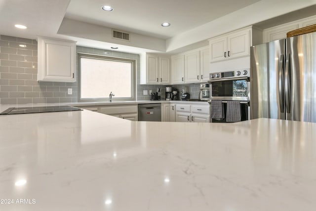 kitchen featuring stainless steel appliances, white cabinetry, light stone countertops, sink, and decorative backsplash