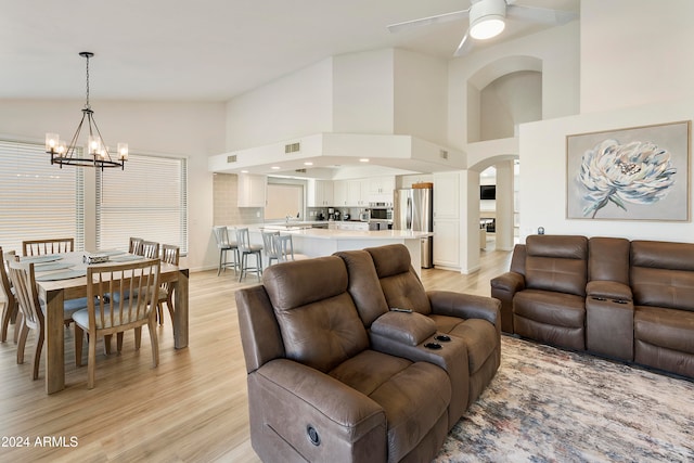 living room featuring ceiling fan with notable chandelier, light hardwood / wood-style flooring, and high vaulted ceiling