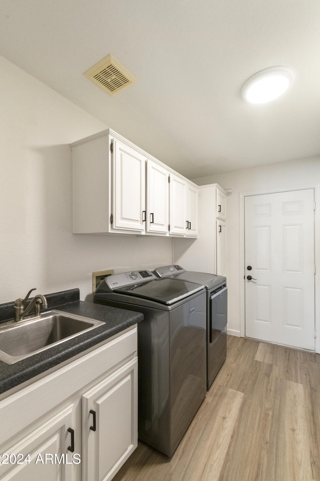 clothes washing area with cabinets, light hardwood / wood-style floors, washer and dryer, and sink