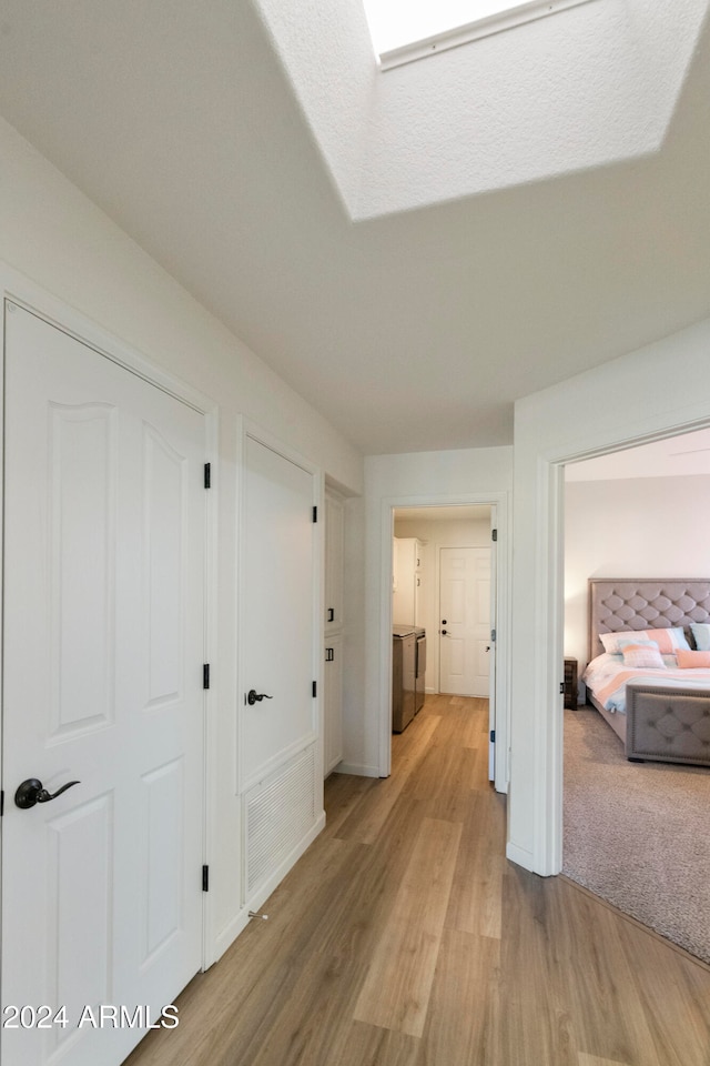 corridor with washer and dryer, a textured ceiling, and light hardwood / wood-style flooring