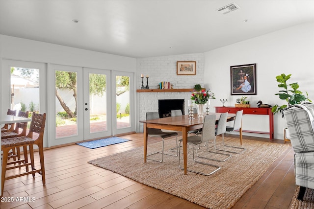 dining space with french doors, hardwood / wood-style floors, and a brick fireplace