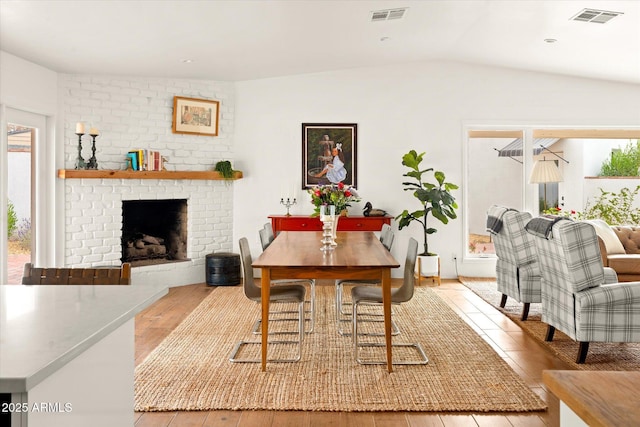 dining area with lofted ceiling, a fireplace, and light wood-type flooring