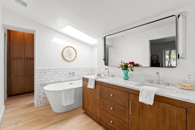 bathroom with a tub to relax in, a skylight, tile walls, vanity, and hardwood / wood-style floors