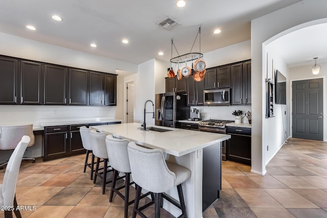 kitchen featuring a kitchen bar, stainless steel appliances, a kitchen island with sink, hanging light fixtures, and sink