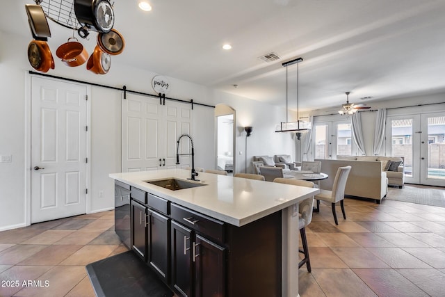 kitchen with ceiling fan, a barn door, a center island with sink, sink, and black dishwasher