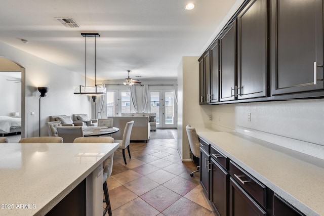 kitchen with ceiling fan, decorative light fixtures, dark brown cabinets, french doors, and light stone counters