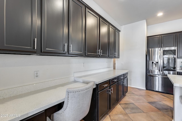 kitchen with light tile patterned flooring, dark brown cabinets, stainless steel fridge, and a breakfast bar