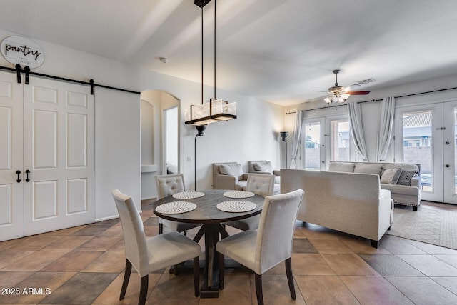 tiled dining space featuring ceiling fan, a barn door, and french doors