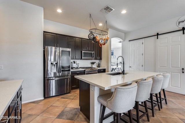 kitchen featuring a barn door, appliances with stainless steel finishes, a kitchen island with sink, a kitchen breakfast bar, and sink