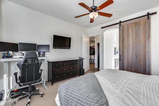 bedroom with ceiling fan, light carpet, and a barn door