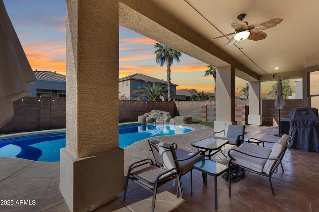 pool at dusk featuring ceiling fan and a patio