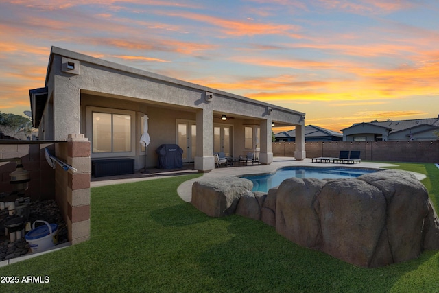 pool at dusk with a lawn, ceiling fan, and a patio