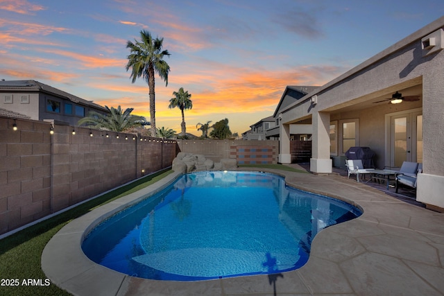 pool at dusk with a patio area, area for grilling, and ceiling fan