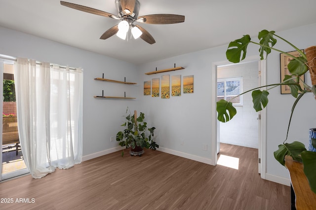 unfurnished room with wood finished floors, a ceiling fan, and baseboards
