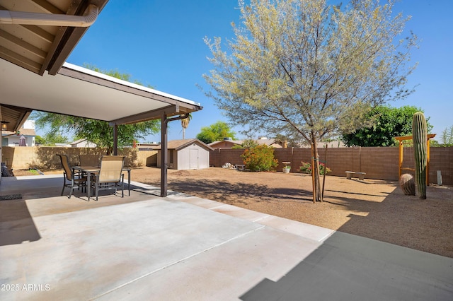 view of patio / terrace featuring a storage unit, a fenced backyard, outdoor dining area, and an outbuilding