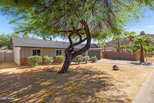 ranch-style house featuring driveway, fence, board and batten siding, an attached garage, and roof with shingles
