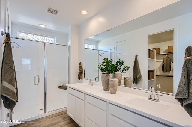 bathroom with a sink, visible vents, wood finished floors, and a shower stall