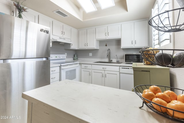 kitchen featuring light stone countertops, white appliances, a tray ceiling, sink, and white cabinets