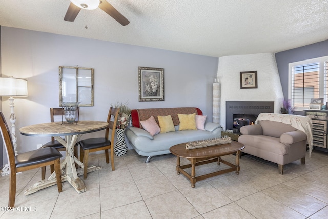 tiled living room with a textured ceiling, ceiling fan, and a large fireplace